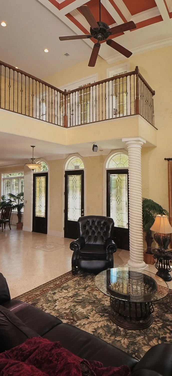 Two-story foyer with coffered ceiling, wrought iron railing, glass doors, and fluted columns